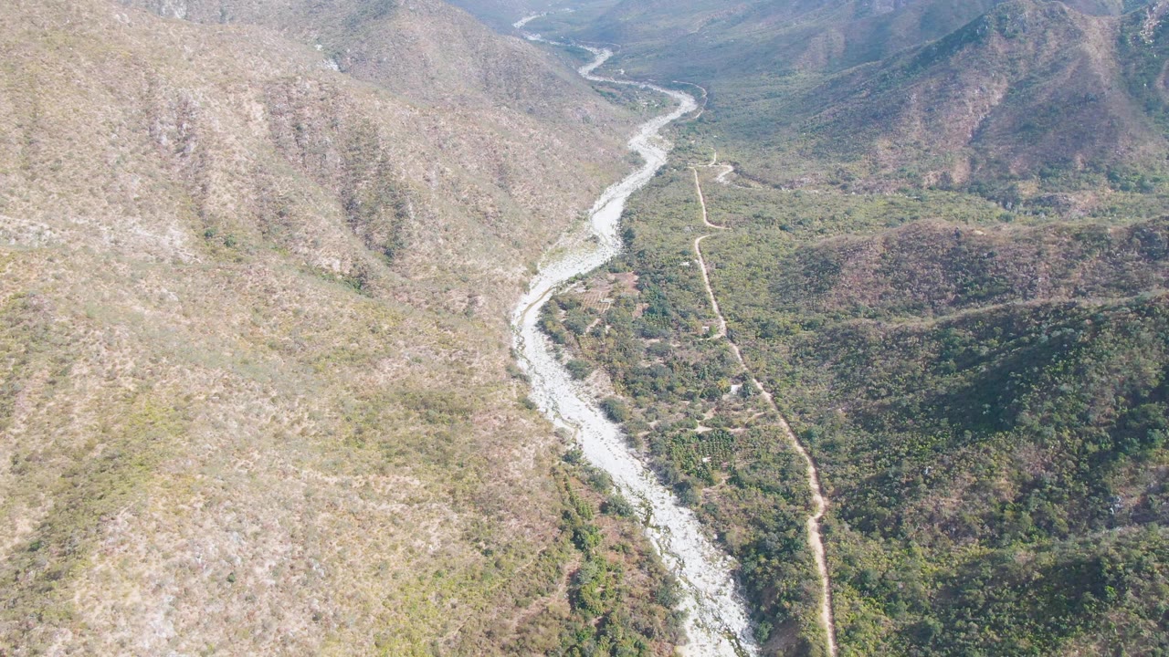 Aerial view in San Dionisio, Baja California Sur with the rocky riverbed running from foreground toward distant hills, a narrow road on the right, and no visible people.
