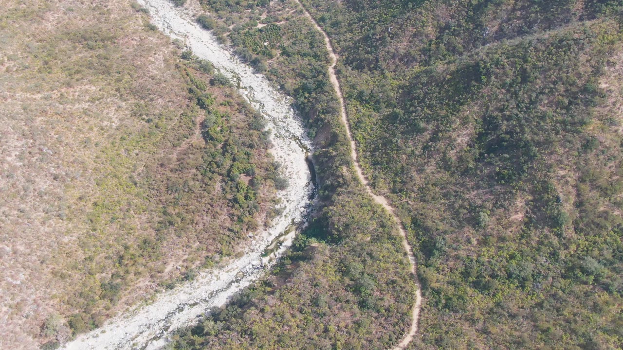 Aerial landscape with a winding riverbed crossing the frame near hilly green vegetation.