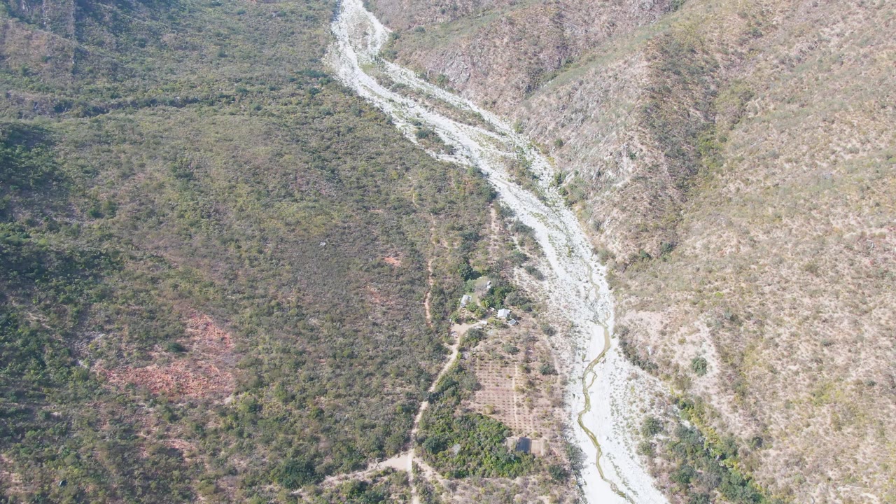 Aerial view over San Dionisio, Baja California Sur, with a pale riverbed curving through scrub-covered rocky slopes and no visible people.