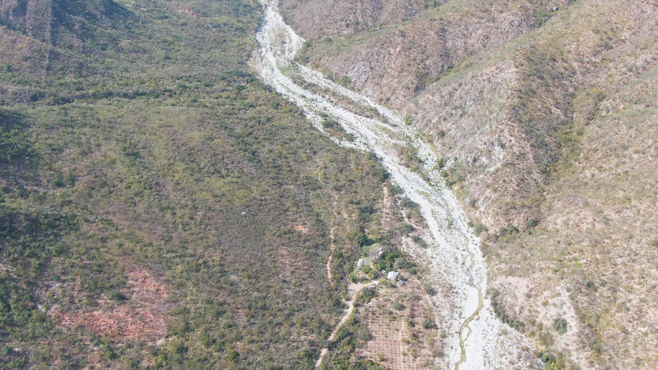 Drone-like overhead view of a rocky valley crossed by a pale river channel.
