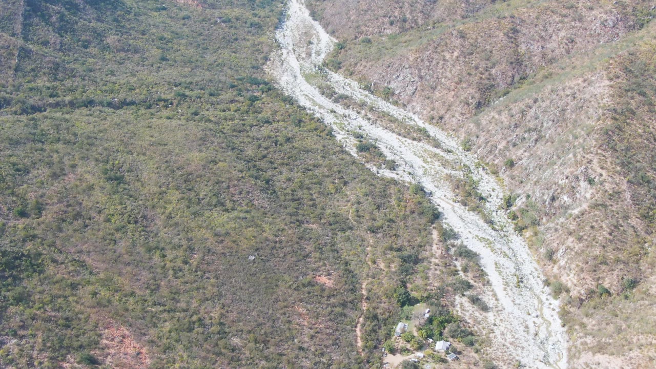 Aerial frame from San Dionisio, Baja California Sur showing a pale winding road or dry wash cutting diagonally through scrub-covered hillsides, with no visible people.