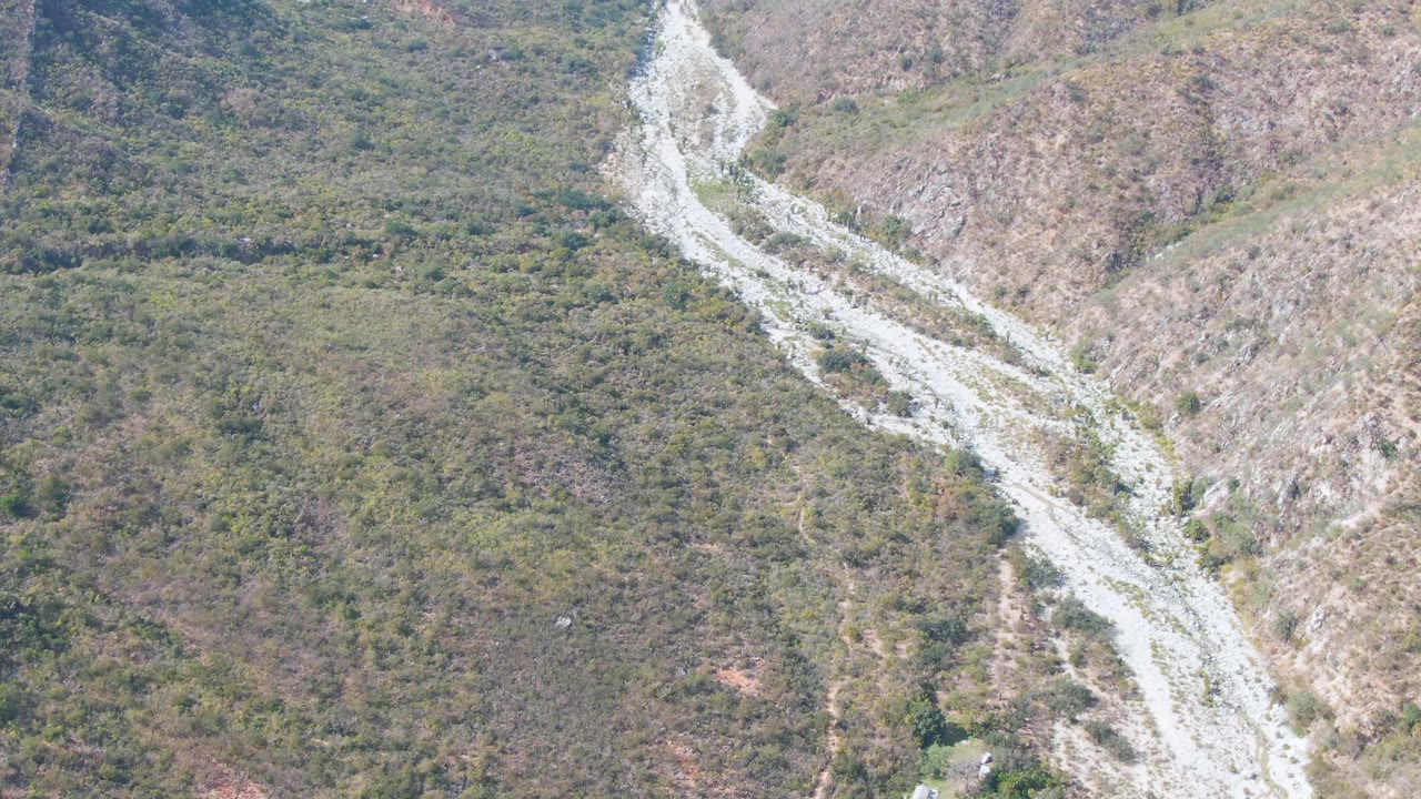 Aerial frame from San Dionisio, Baja California Sur showing the pale winding route slightly shifted across dense scrub patches and rocky brown slopes, with no visible people.
