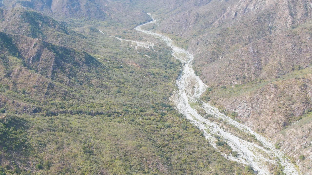 Aerial view of a pale riverbed winding through green and brown mountains