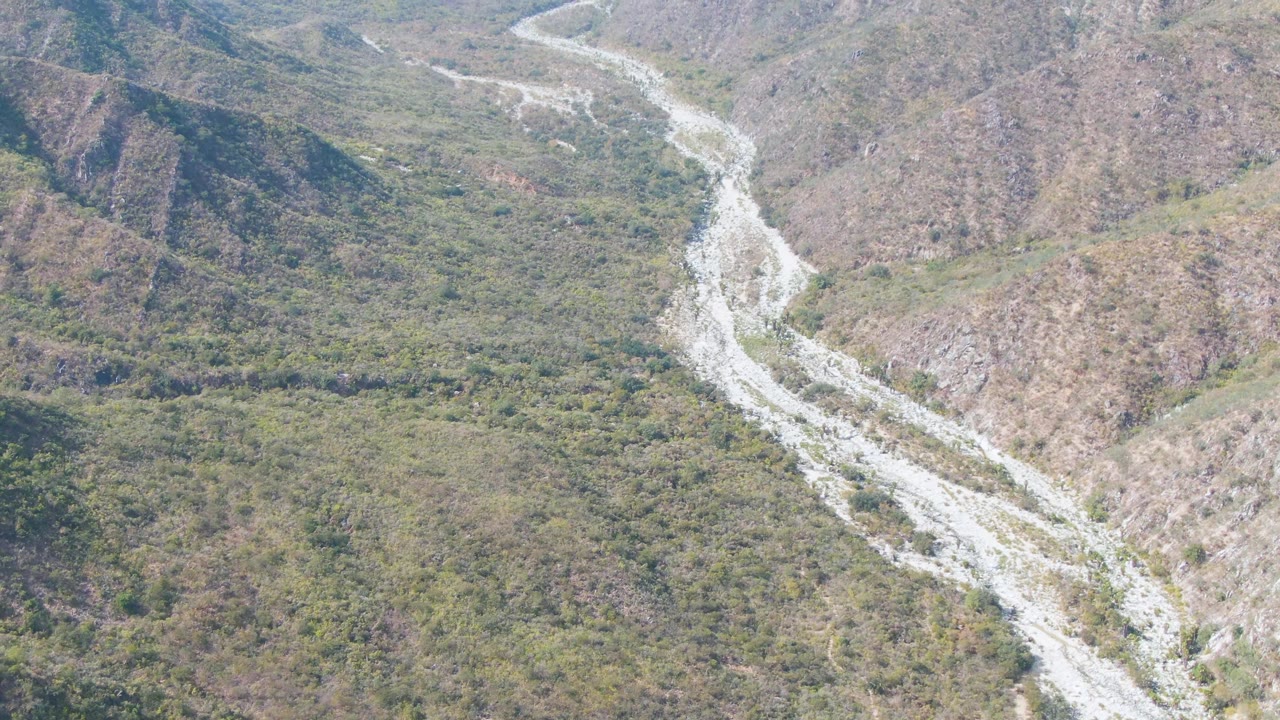 Aerial frame from San Dionisio, Baja California Sur, with the riverbed running from upper frame into the lower valley across scrub-covered terrain and no visible people.