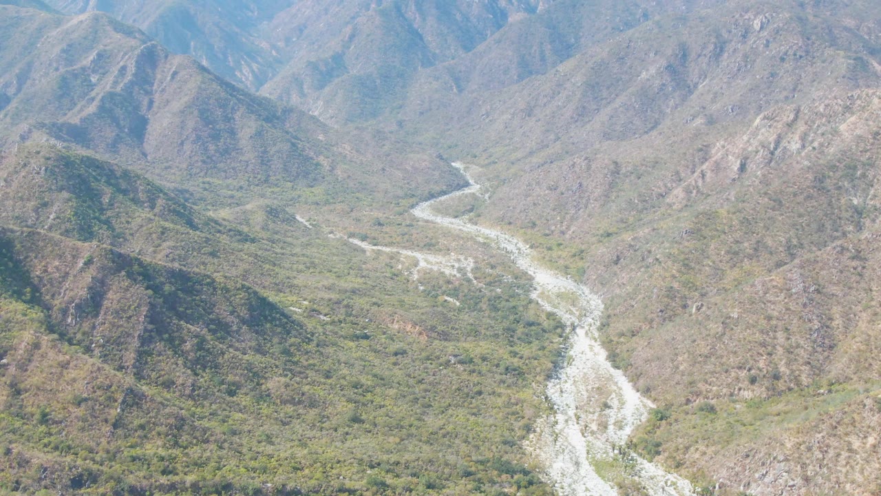 Aerial view of a pale river winding through a rocky mountain valley.