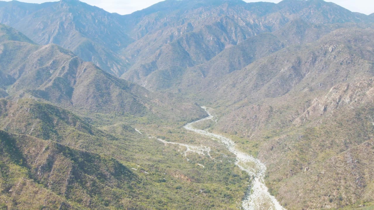 San Dionisio mountain valley frame with the pale riverbed bending through the lower center and a lighter patch of sky above the ridgeline, with no visible people.
