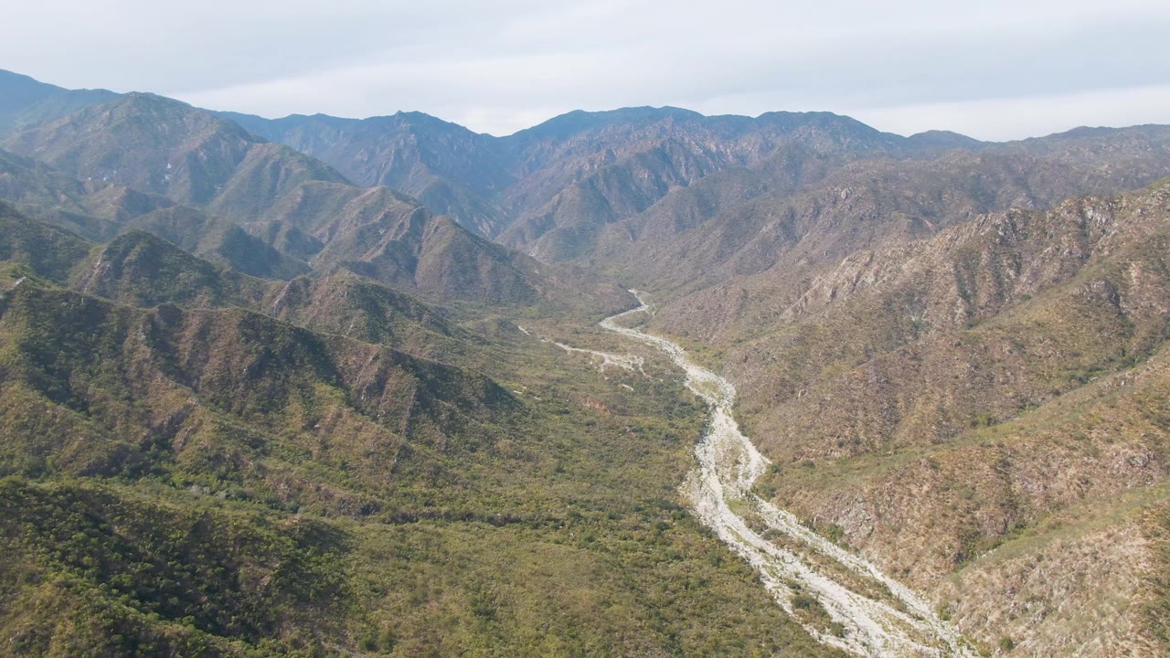 Mountain valley aerial with riverbed curving through brush.