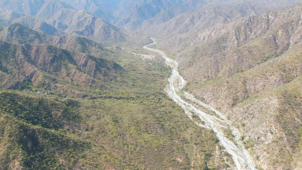 Aerial view in San Dionisio, Baja California Sur with the riverbed slightly more centered between brown ridges and green valley vegetation, with no visible people.