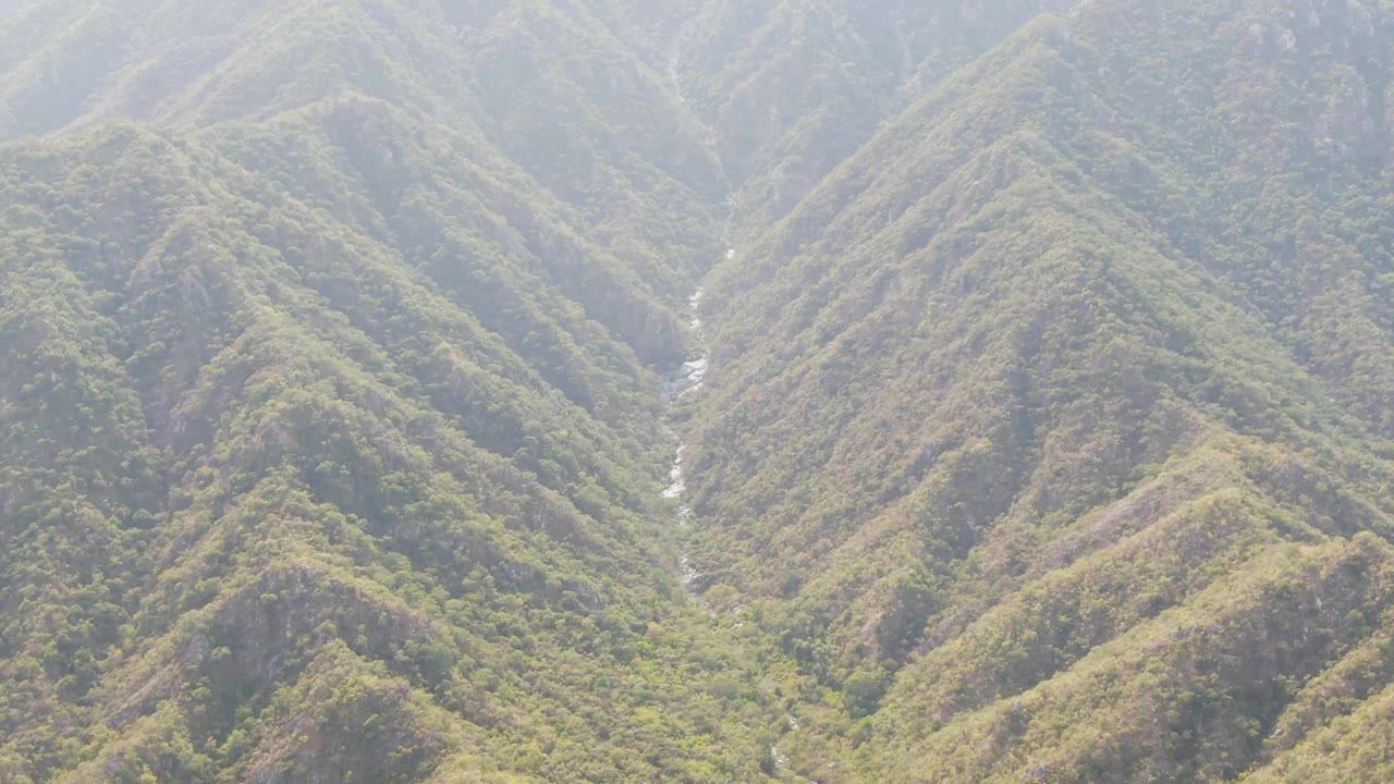 Green mountain ridges with a narrow stream in a hazy valley