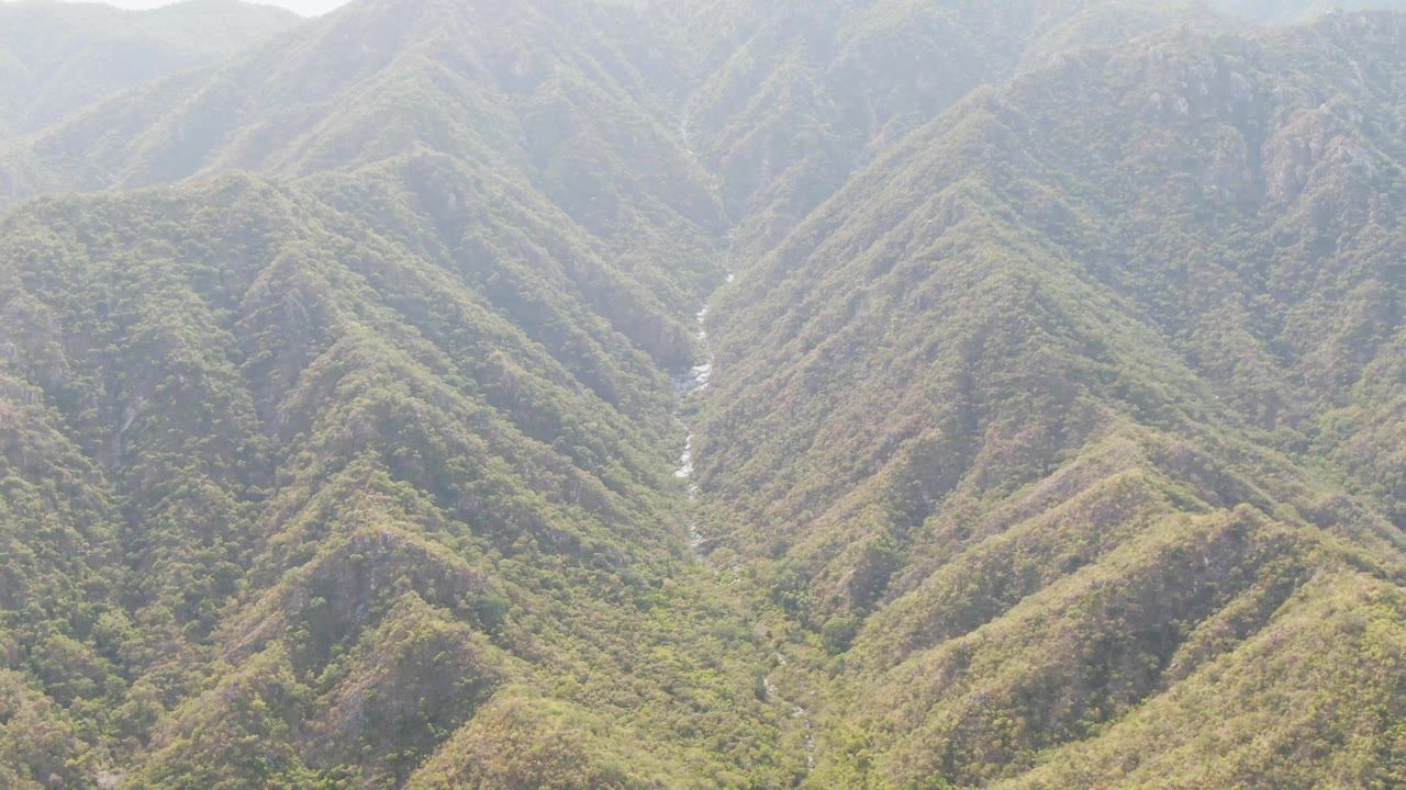 San Dionisio mountain valley seen from above, with a small river channel partly visible between vegetated ridges and no visible people.