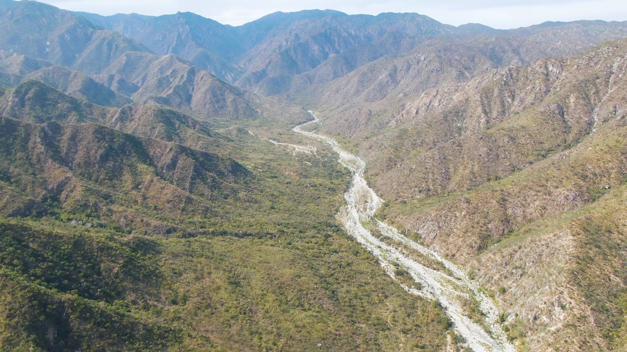 River channel curves through a broad mountain valley under clear sky.