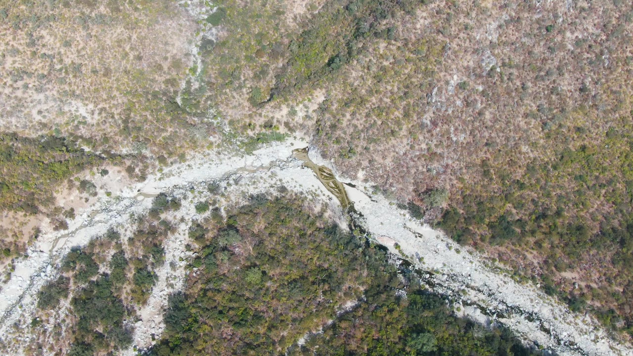 Overhead view of a pale rocky riverbed cutting through green and brown vegetation in San Dionisio, Baja California Sur, with no visible people.