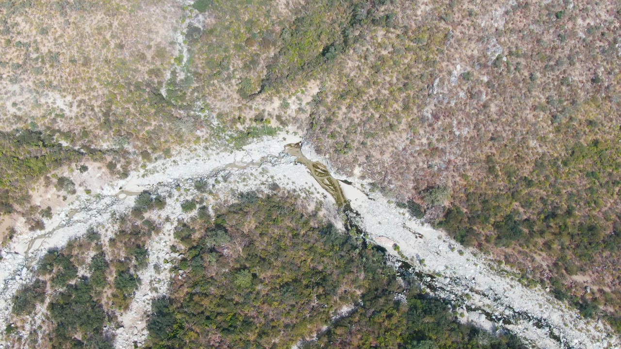 Aerial river channel with white water beside dry brush.