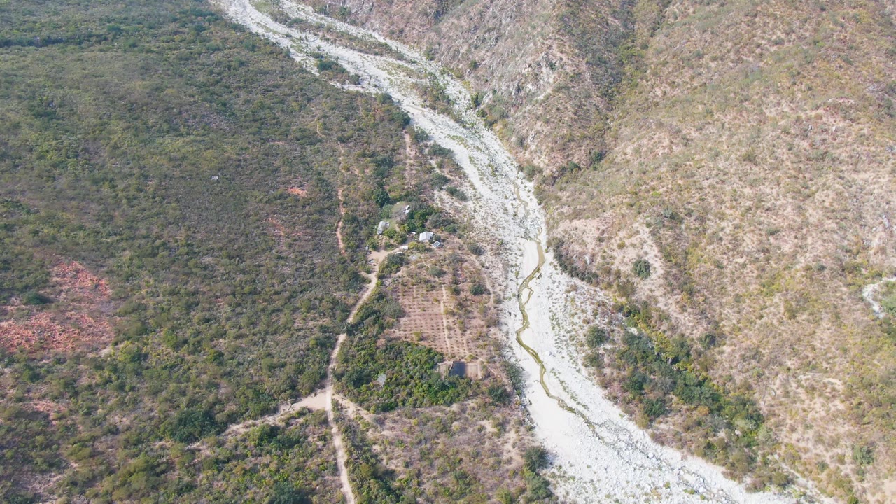 Overhead San Dionisio frame with the river channel centered more vertically, green vegetation to the left, dry slope to the right, and no visible people.