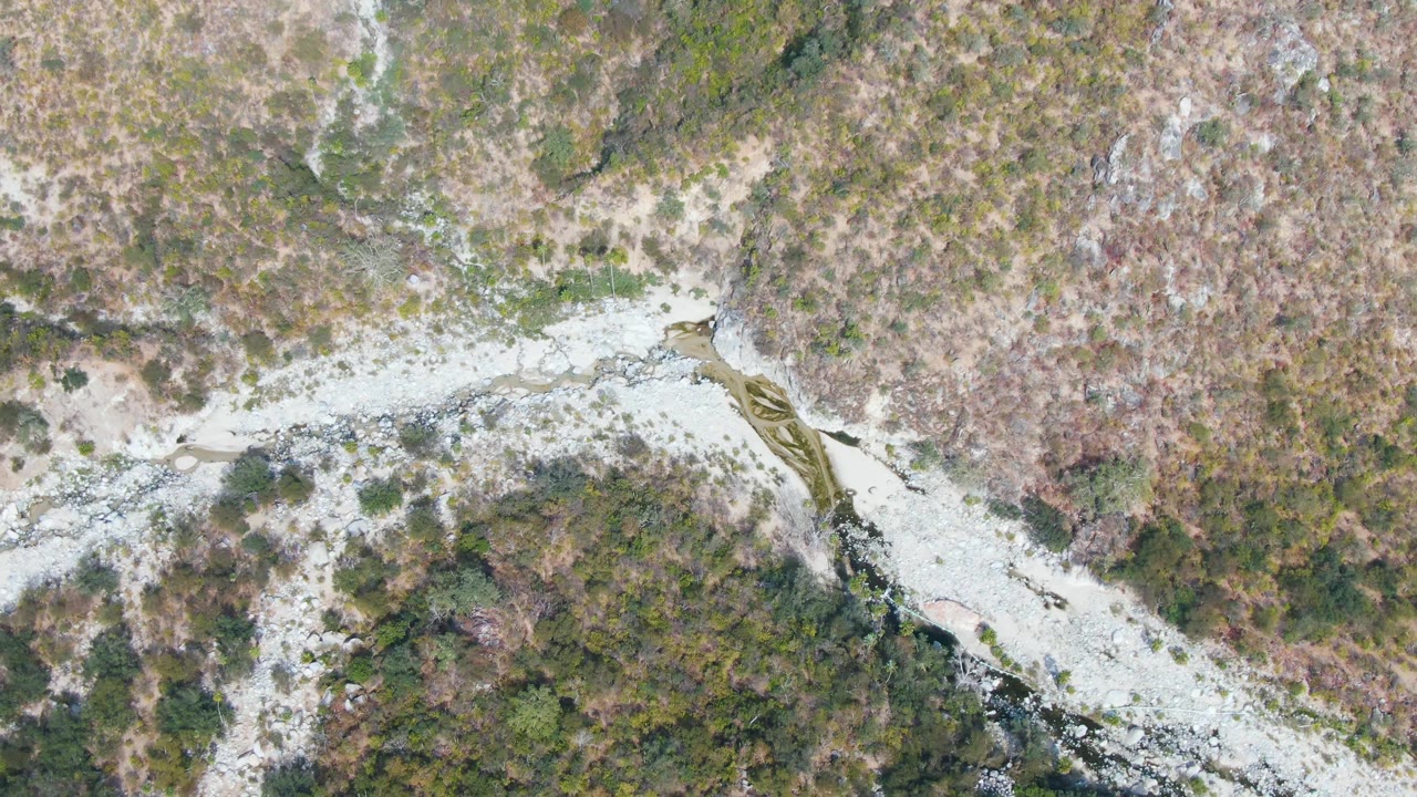 Aerial frame from San Dionisio, Baja California Sur, Mexico, with the light-colored stream bed centered between scrub-covered slopes and no visible people.