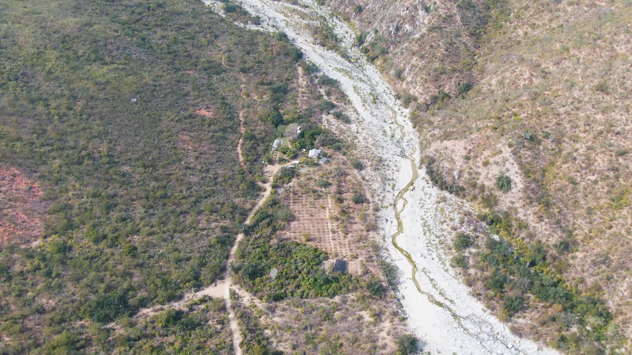 Drone view of dry river channel passing farmland and brush
