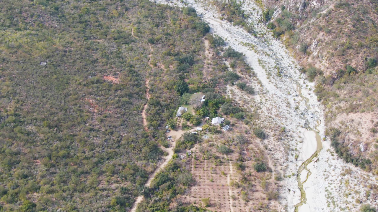 Aerial landscape with scrub forest, farm plots, and a pale rocky wash.