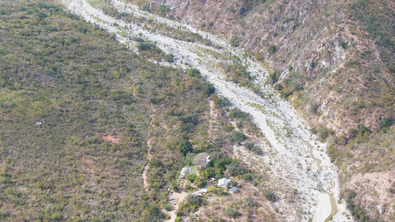 Aerial frame over San Dionisio, Baja California Sur showing a pale winding gravel route between scrub-covered hills and rocky slopes, with no visible people.