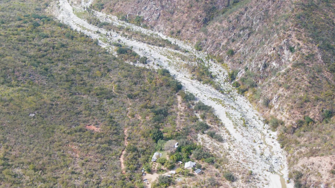 Elevated view of a curving gravel road or wash below rocky green-brown hills.