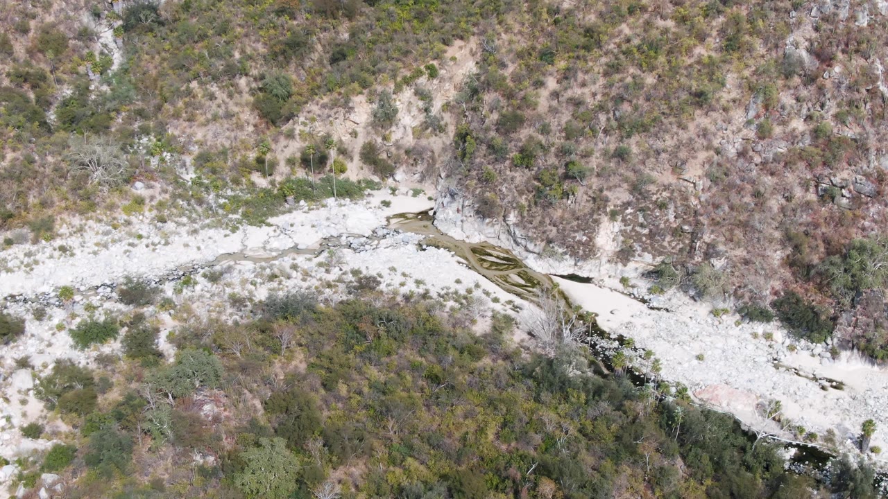 Overhead frame from San Dionisio, Baja California Sur, showing the stream bend sliding along a scrubby hillside with pale rock, brown brush, and no visible people.