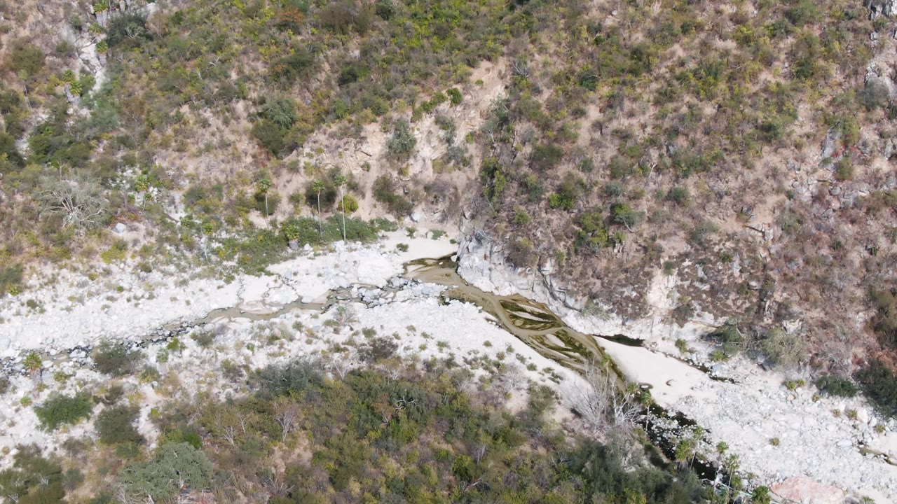Overhead view of a pale rocky riverbed crossing scrubby valley slopes.