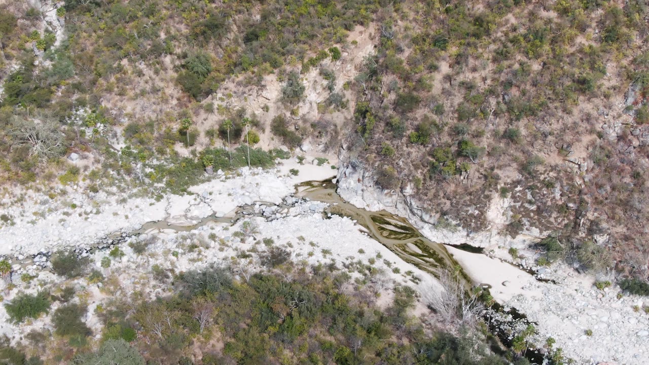 Aerial frame from San Dionisio, Baja California Sur showing the diagonal river channel, pale gravel, patchy shrubs, and no visible people.