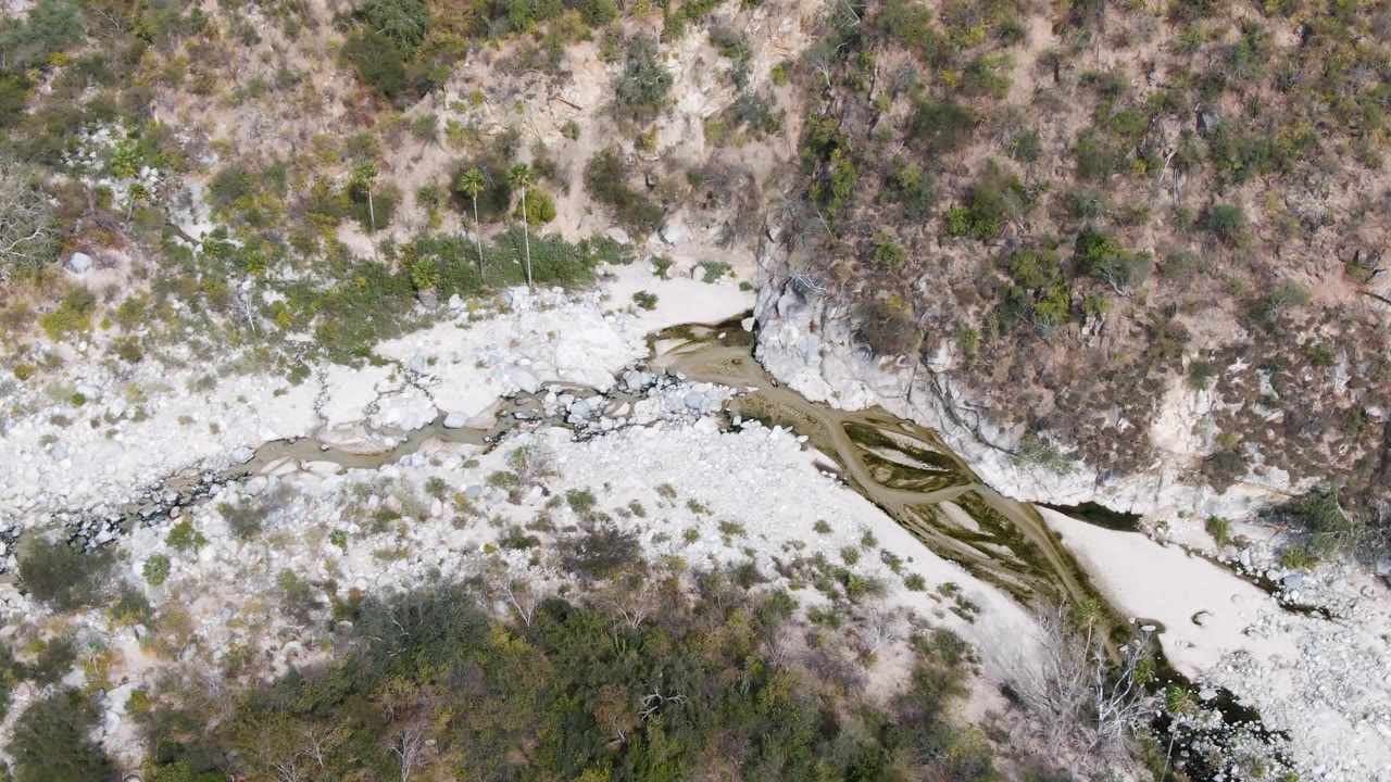 Second overhead frame from San Dionisio, Baja California Sur with the sediment-filled riverbed pressed against a brushy hillside and no visible people.
