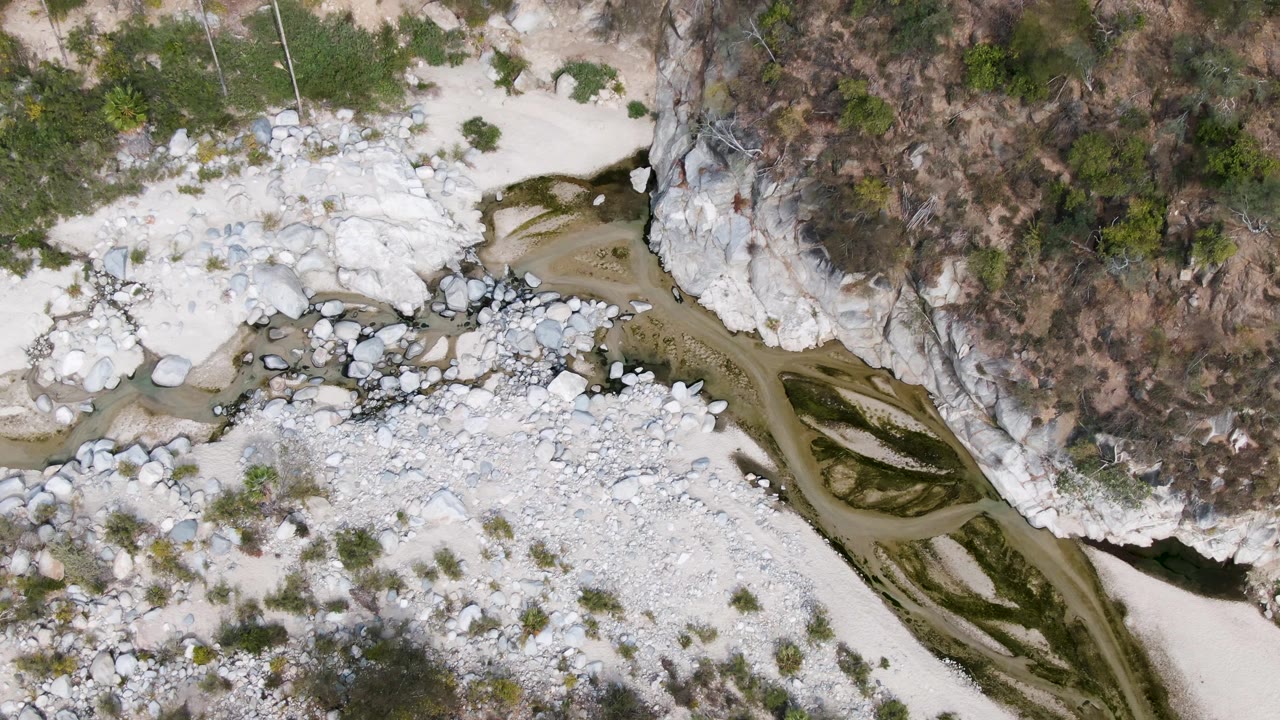 Aerial river channel cutting through pale rocks and sand near a cliff.