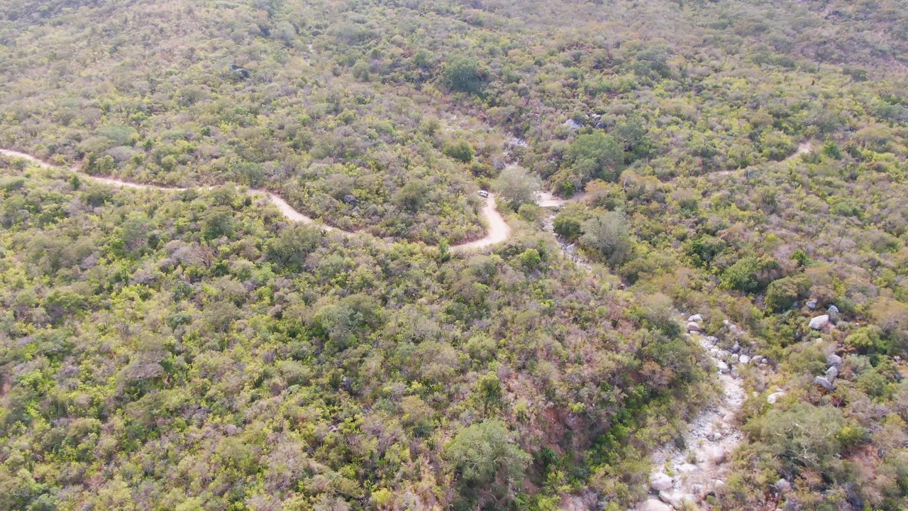 Aerial view in San Dionisio, Baja California Sur with the winding road across the upper hillside and a stony riverbed cutting through the lower frame, with no visible people.