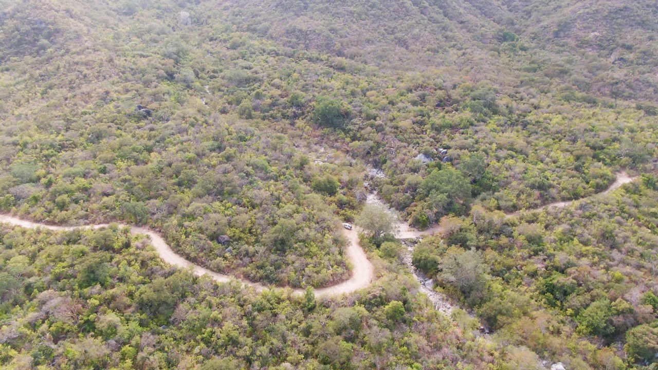 Aerial view of a winding dirt road through green hillside vegetation.