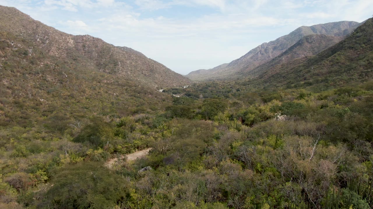 Second frame of the San Dionisio aerial view, showing the valley corridor between rocky slopes, dense desert brush in the lower frame, and no visible people.