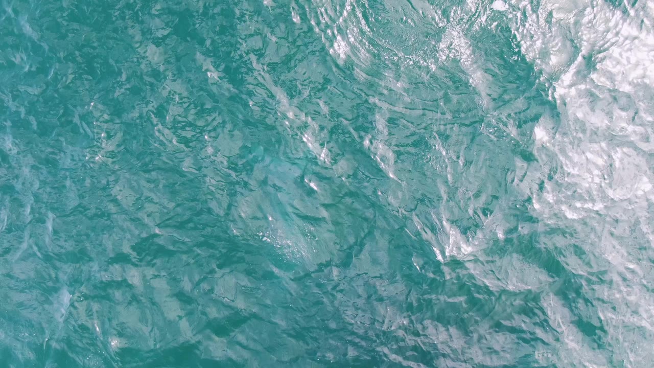 Overhead turquoise ocean water with white wake texture.