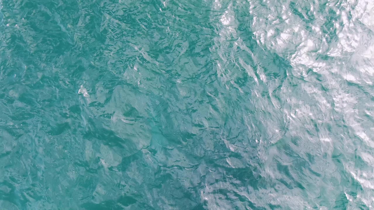 Top-down frame of turquoise ocean at Shipwrecks, Baja California Sur, showing pale white wake and layered ripple patterns across the water with no visible people.