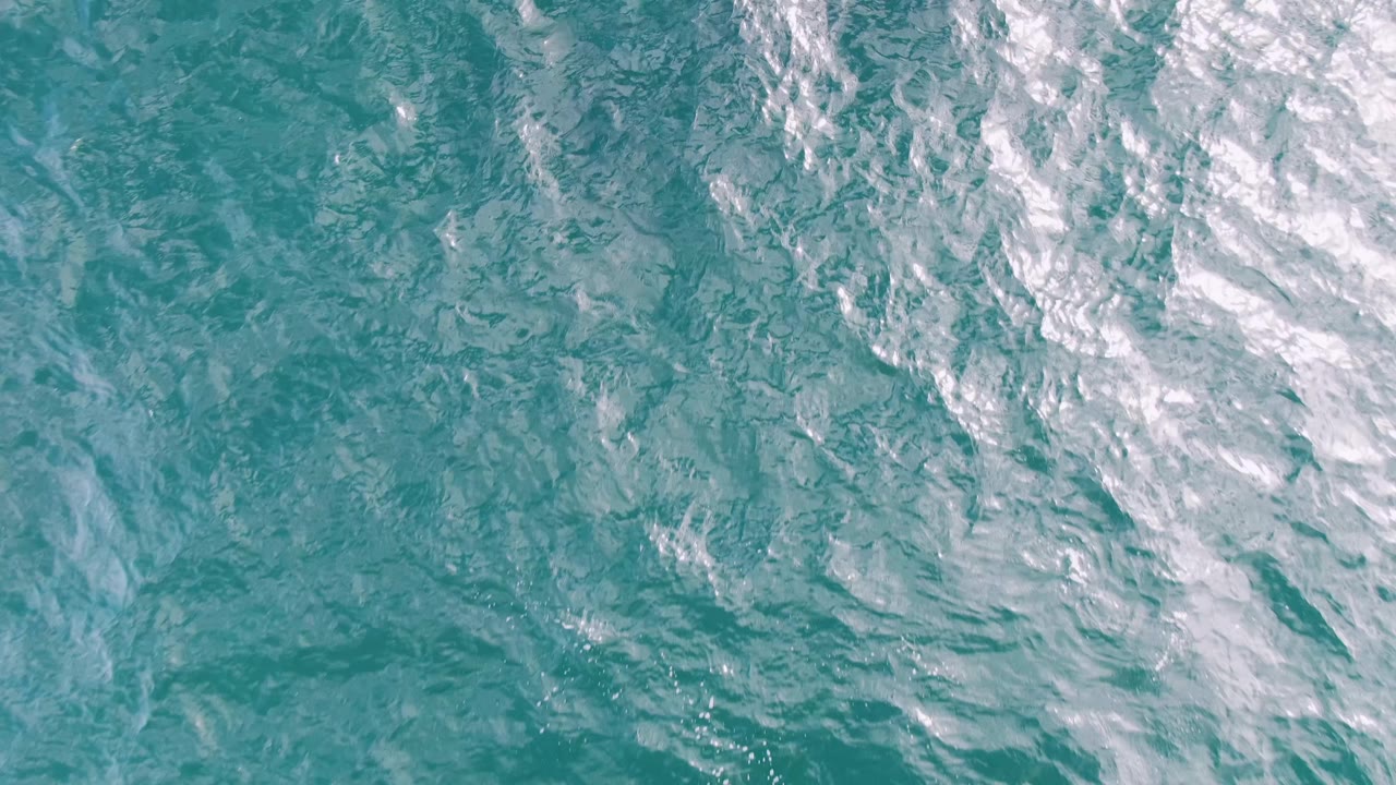 Aerial frame over Shipwrecks, Baja California Sur, showing rippled turquoise water with a broader white foam band across the upper right and no visible people.