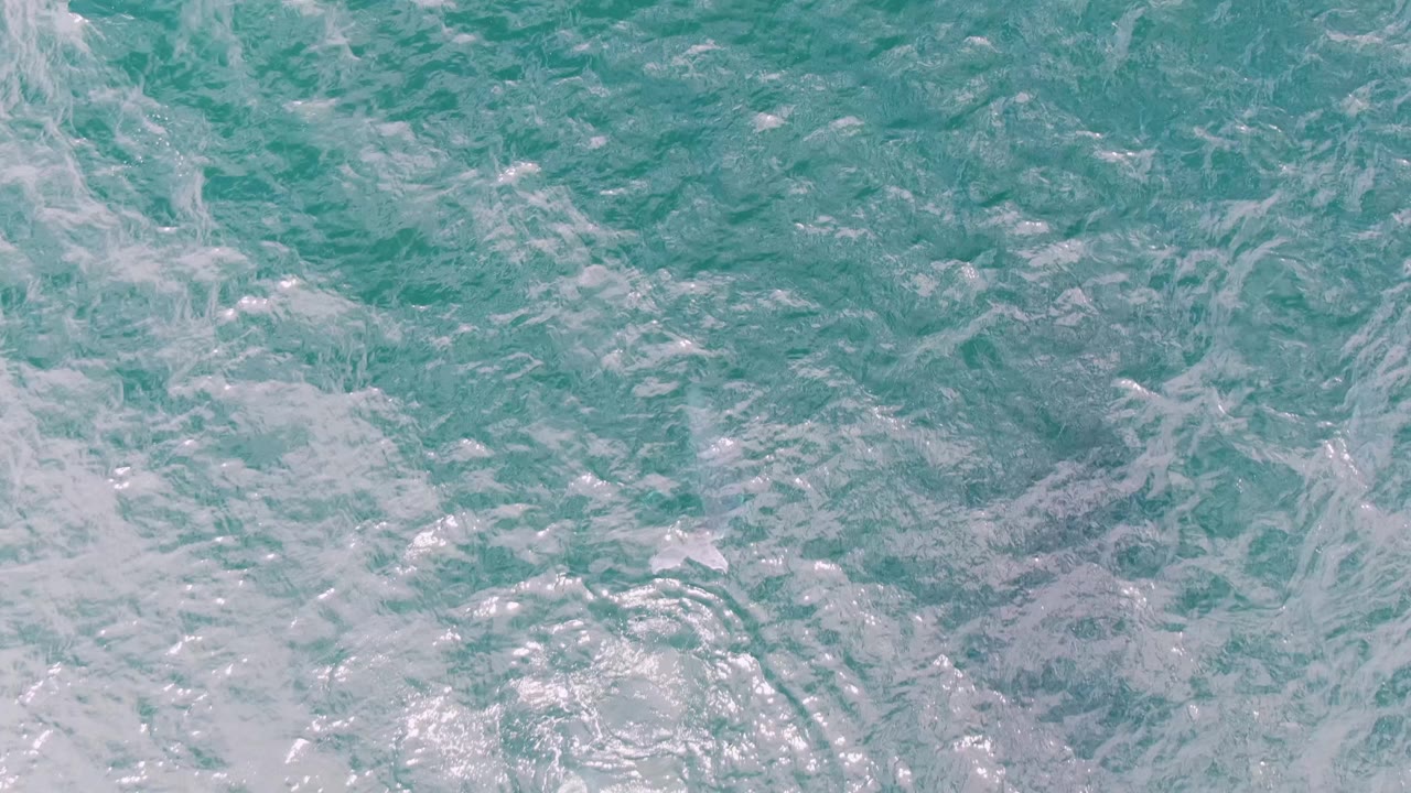 Aerial ocean surface at Shipwrecks, Baja California Sur, showing pale foam swirls over blue-green water with no visible people or vessels.