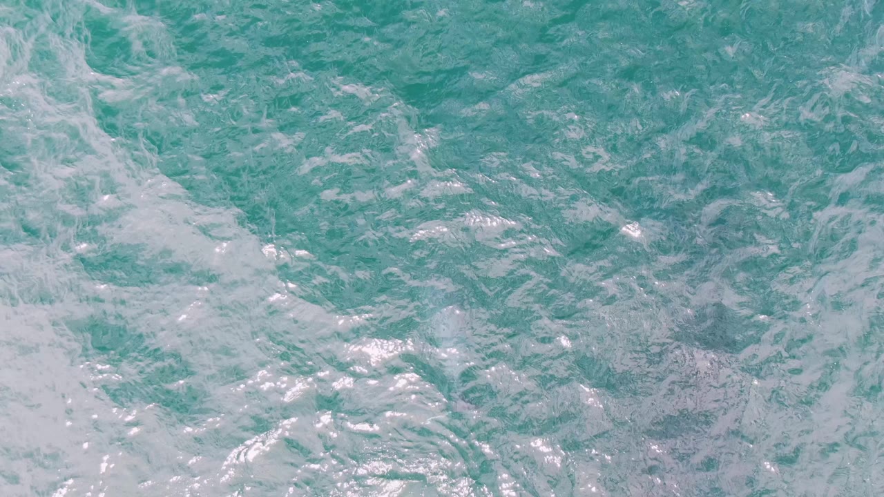 Top-down view of Shipwrecks, Baja California Sur ocean water, with denser white foam trails crossing the turquoise surface and no visible people.