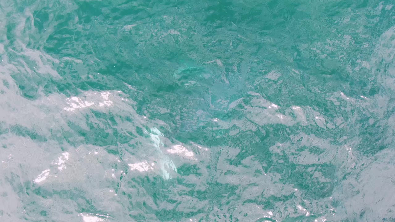 Top-down view of turquoise sea at Shipwrecks with wider white foam bands spread across rippled water, no visible people.