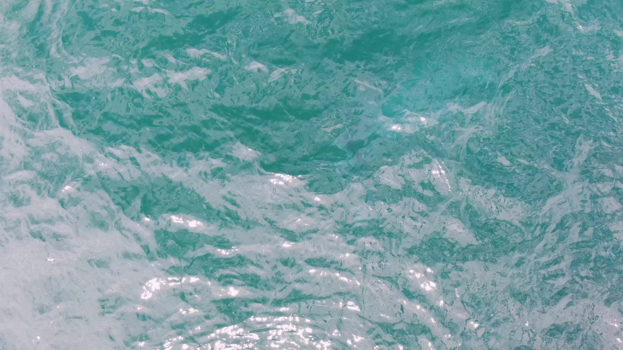 Overhead ocean detail at Shipwrecks with pale foam drifting across textured turquoise ripples and no land or people visible.