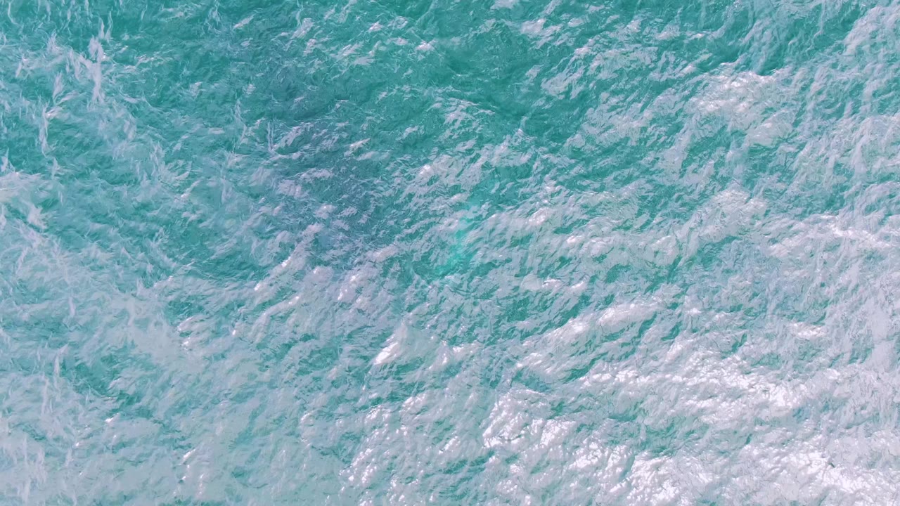 Overhead view of turquoise water and scattered white foam at Shipwrecks, Baja California Sur, with no visible people.