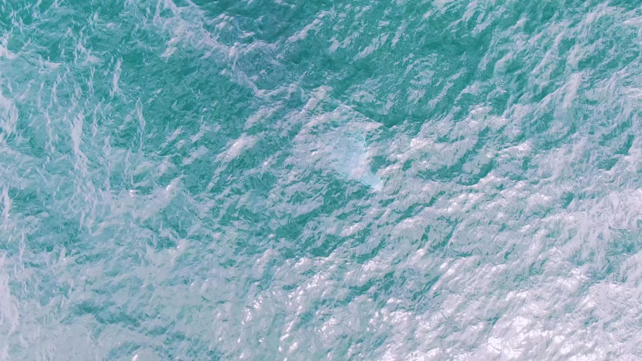 Overhead frame of choppy turquoise sea and pale foam patches at Shipwrecks, Baja California Sur, Mexico, with no visible people.