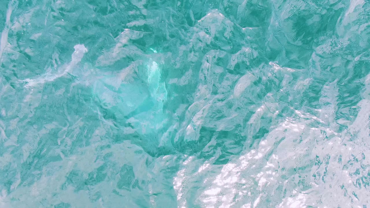 Overhead view of bright aqua water at Shipwrecks East Cape BCS with cloudy white splash texture concentrated through the middle and no visible people.