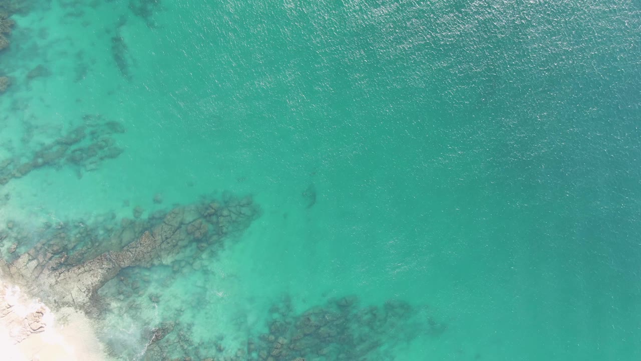 Clear green-blue water over rocks beside a small sandy shore
