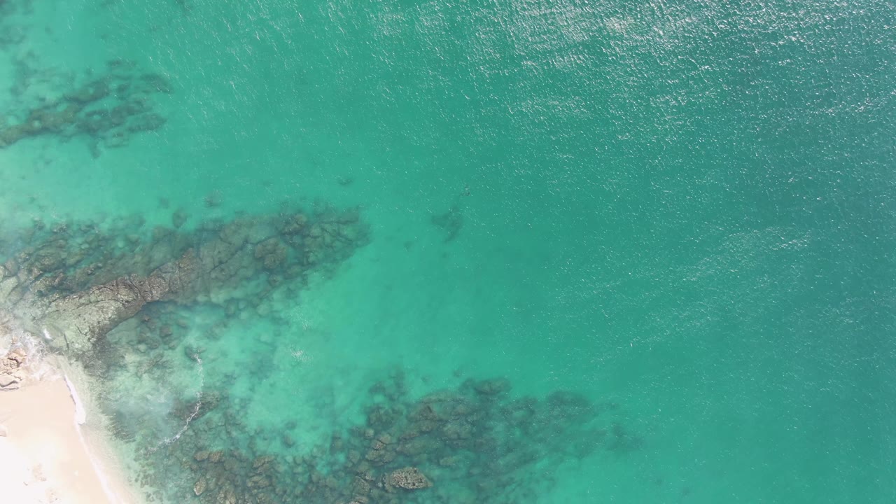 At 0:01, the Buzzards Beach shoreline remains at the lower left while clear turquoise water reveals submerged rock patches, with no visible people.