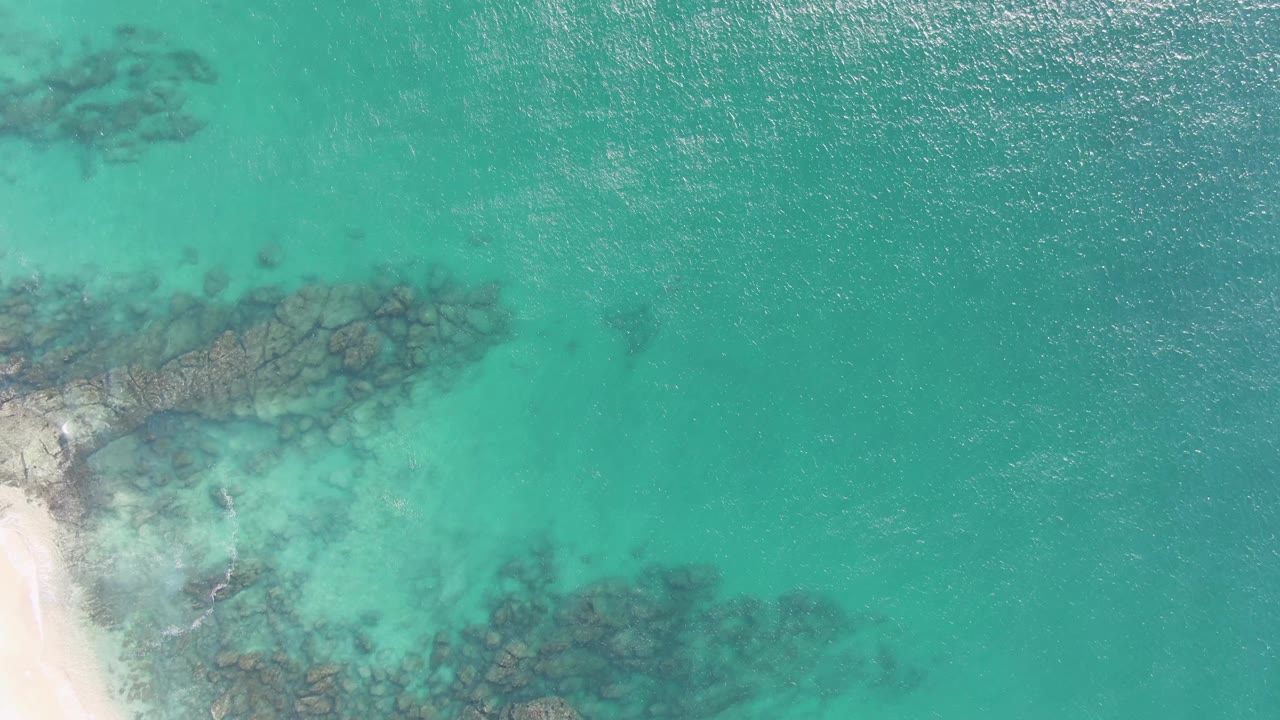 Overhead turquoise water with submerged rocks and a small strip of sand.