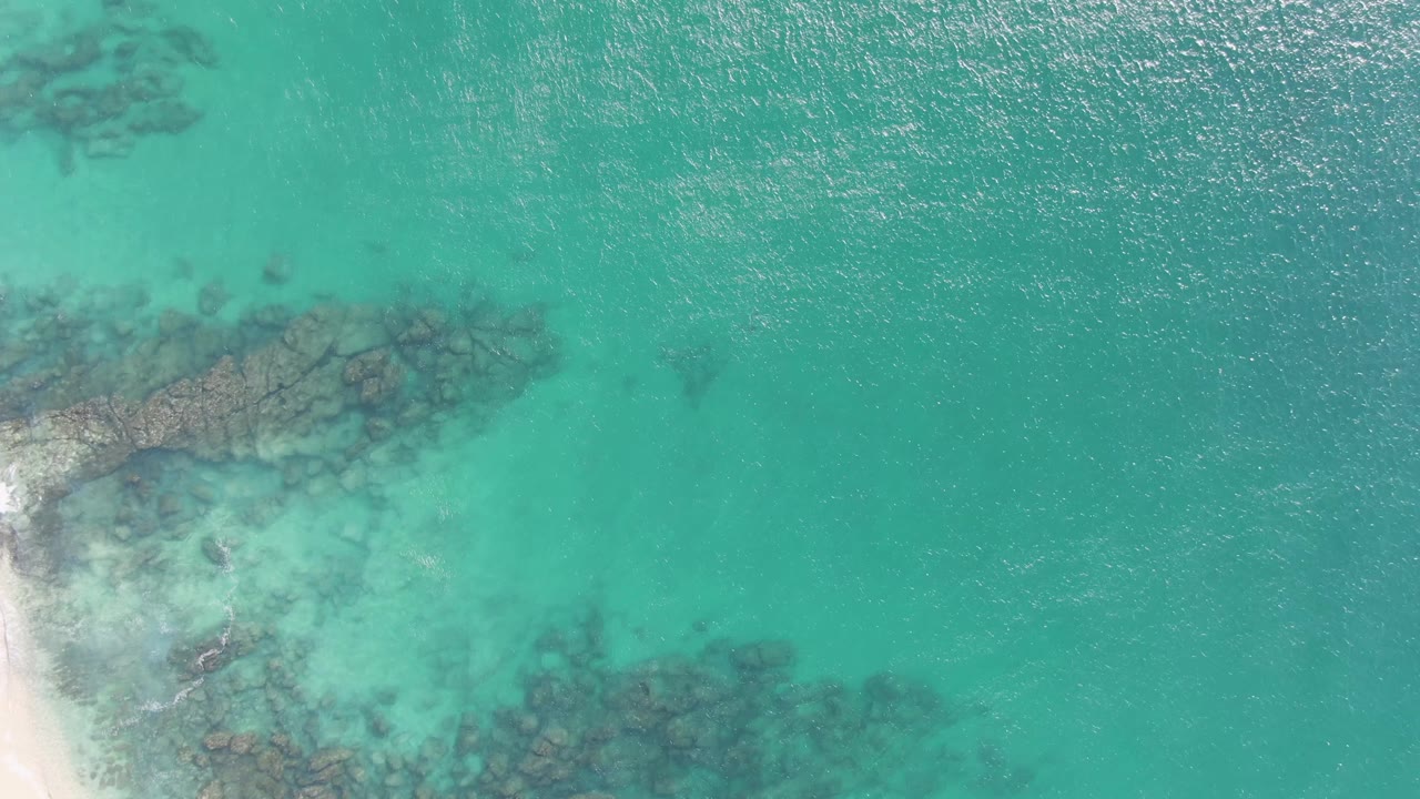 Third frame from Buzzards Beach in Baja California Sur showing more open turquoise water, scattered dark rock patches beneath the surface, and no visible people.