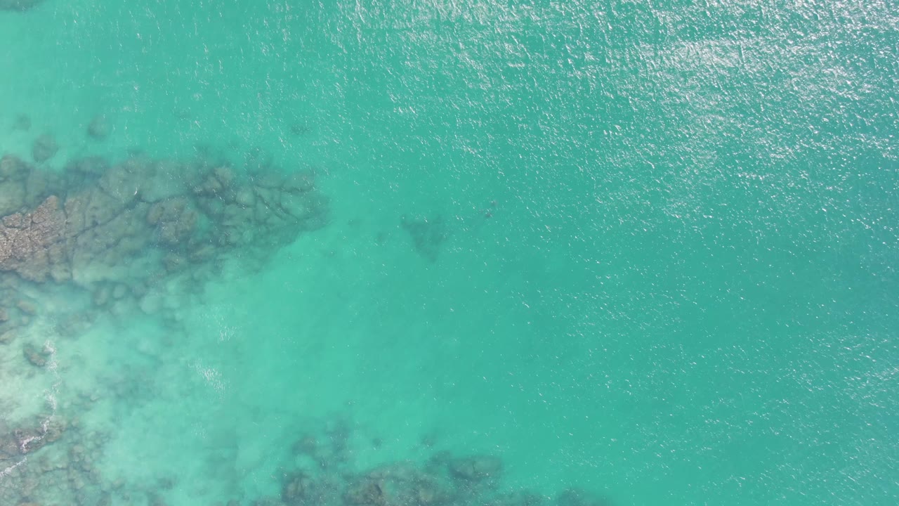 Overhead view of clear turquoise water at Buzzards Beach, Baja California Sur, with submerged rock shapes along the left side and no visible people.