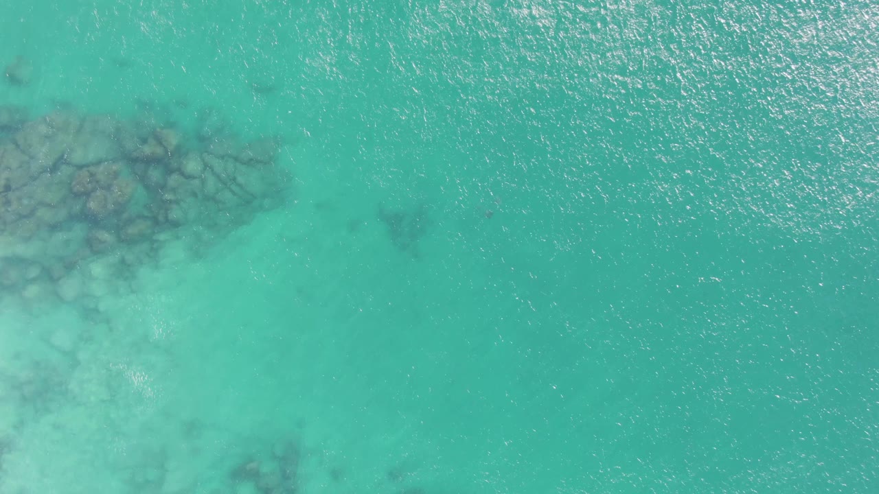 Clear Buzzards Beach ocean water with a dark reef-like rock cluster near the top center and brighter rippled water across the right side, with no visible people.