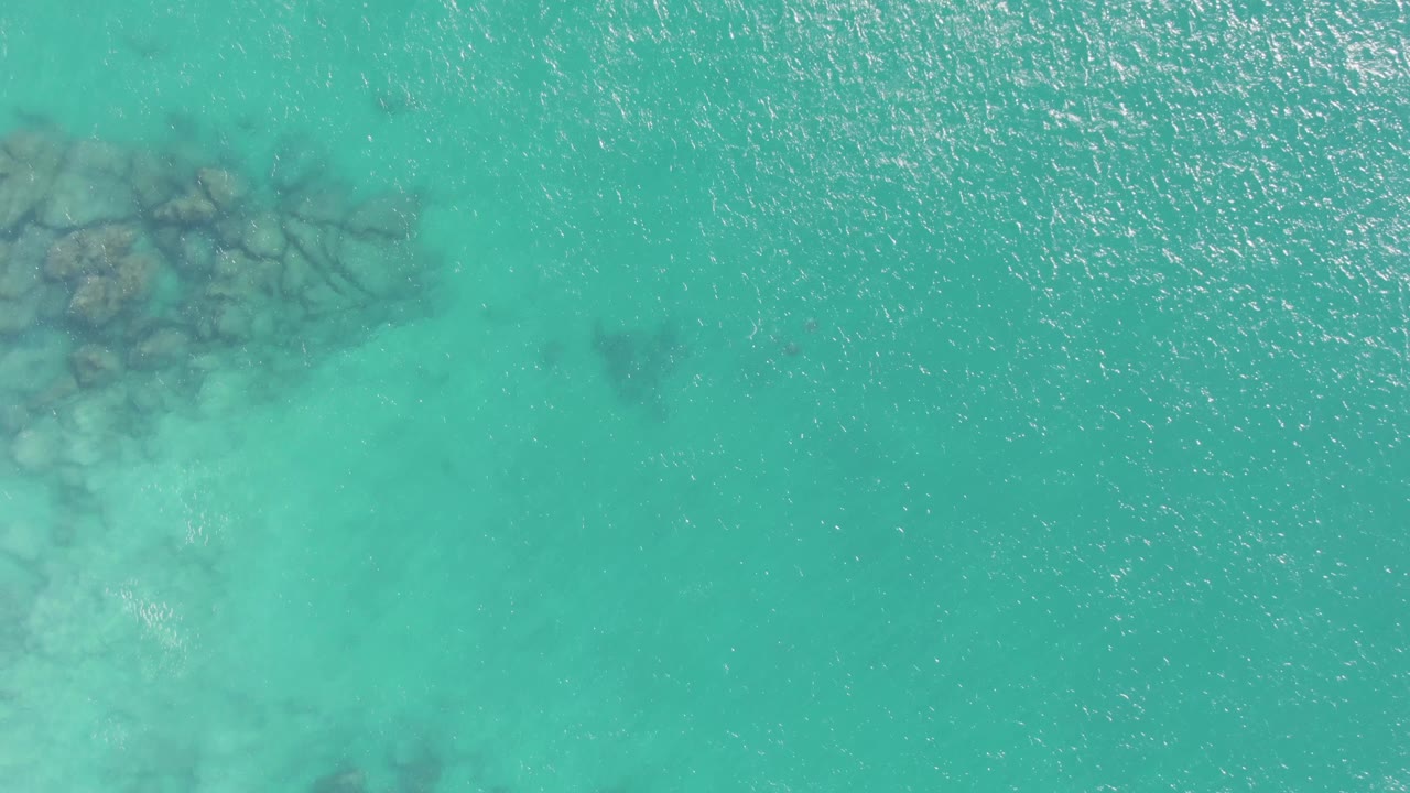 Turquoise water with submerged rocks clipped along the left edge.