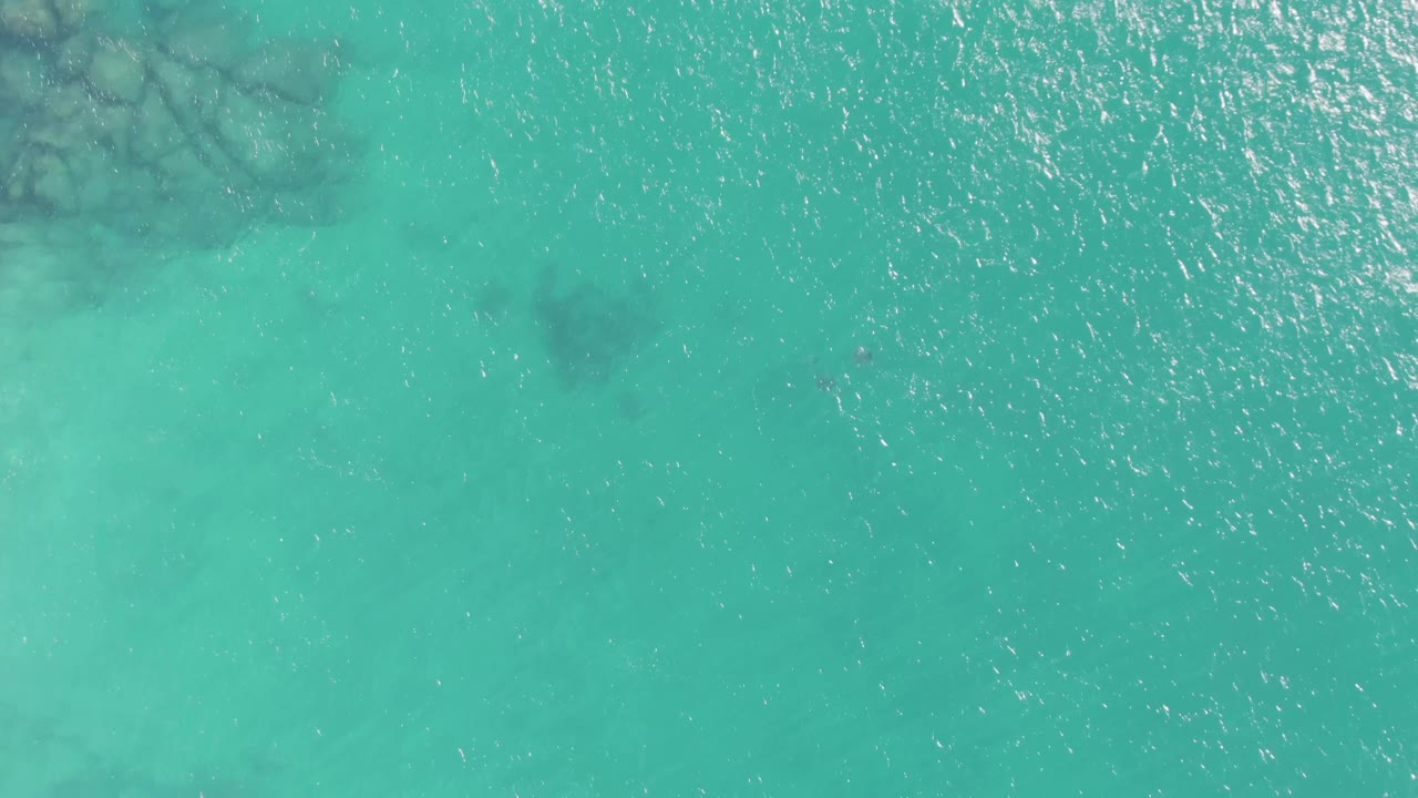 Overhead view of turquoise water at Buzzards Beach, Baja California Sur, with scattered darker sea-floor patches and no visible people.