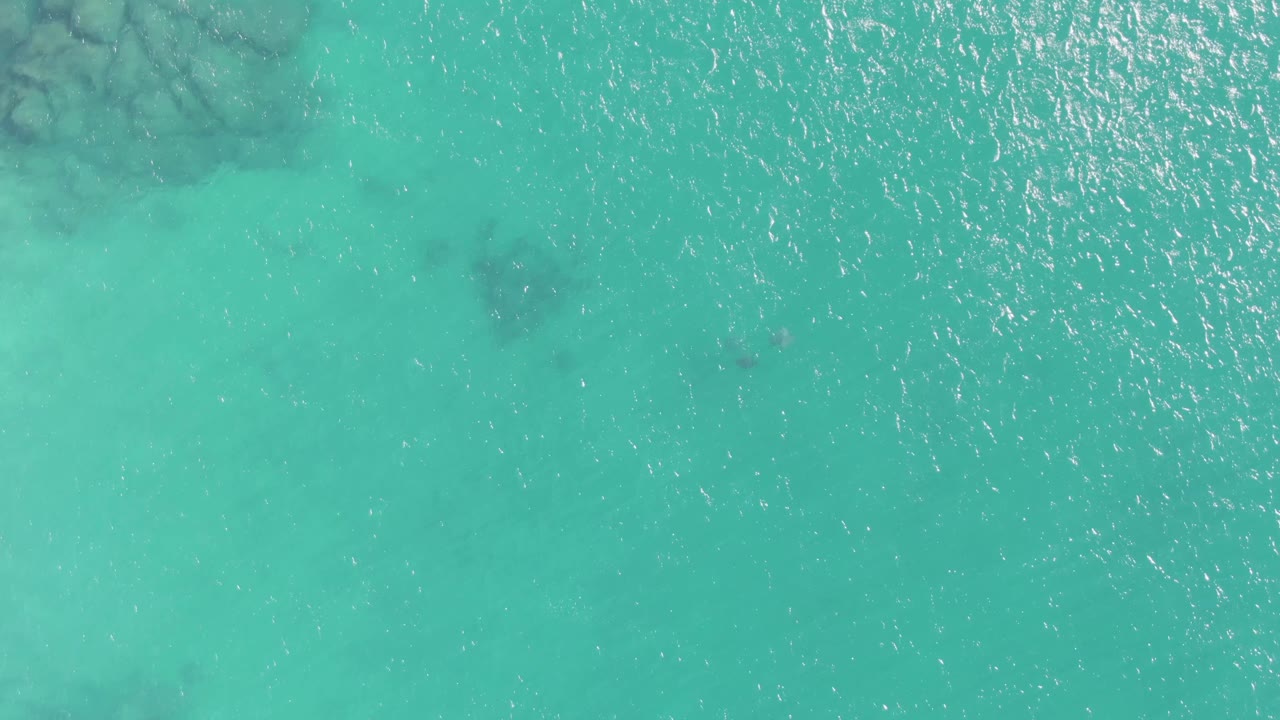 Clear turquoise water with bright ripples and faint dark patches below.